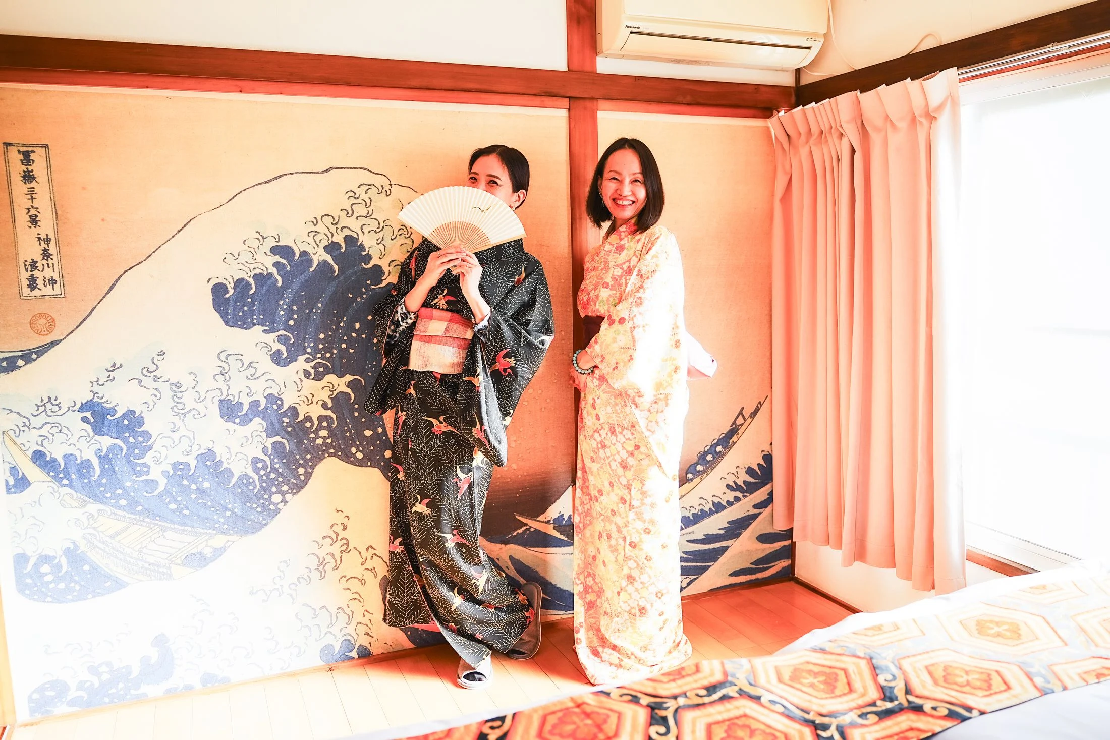 Two guests in kimono in front of the Great Wave mural